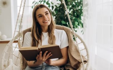 Young woman relaxing on hanging chair reading a book and looking away